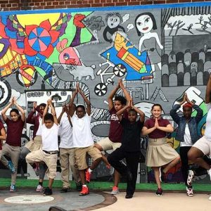 Students at Sussex Avenue School stand in front of a playground mural created during an AIE residency.